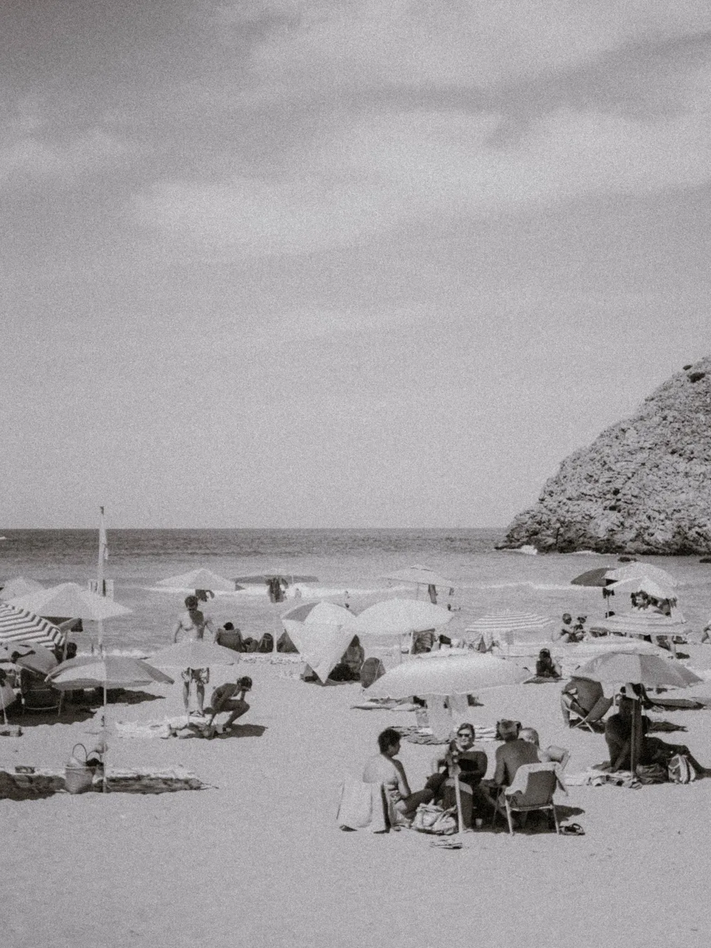 Grainy black and white beach scene with rows of parasols and a rocky headland