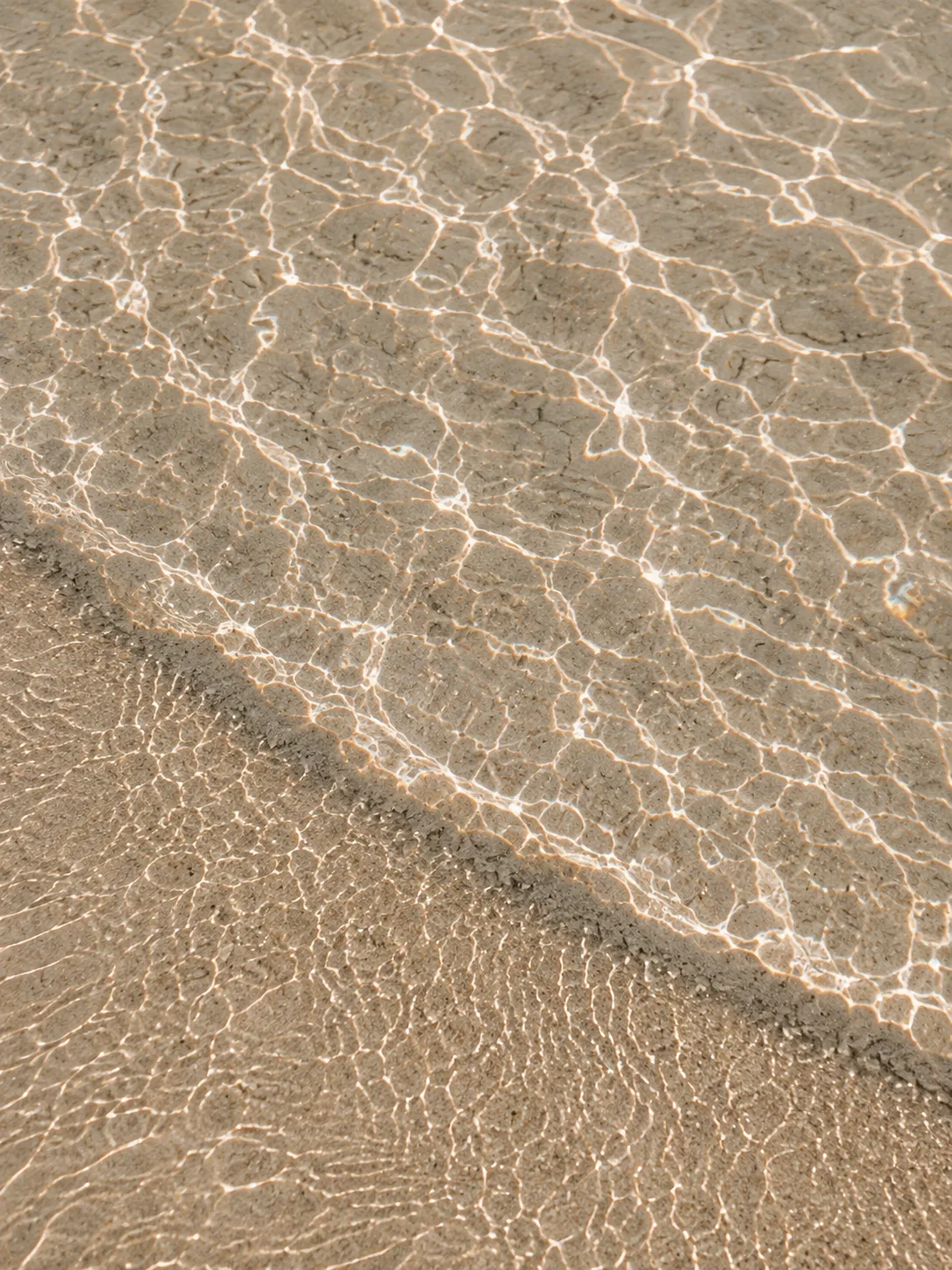 Sunlight rippling through clear shallow water over golden sand