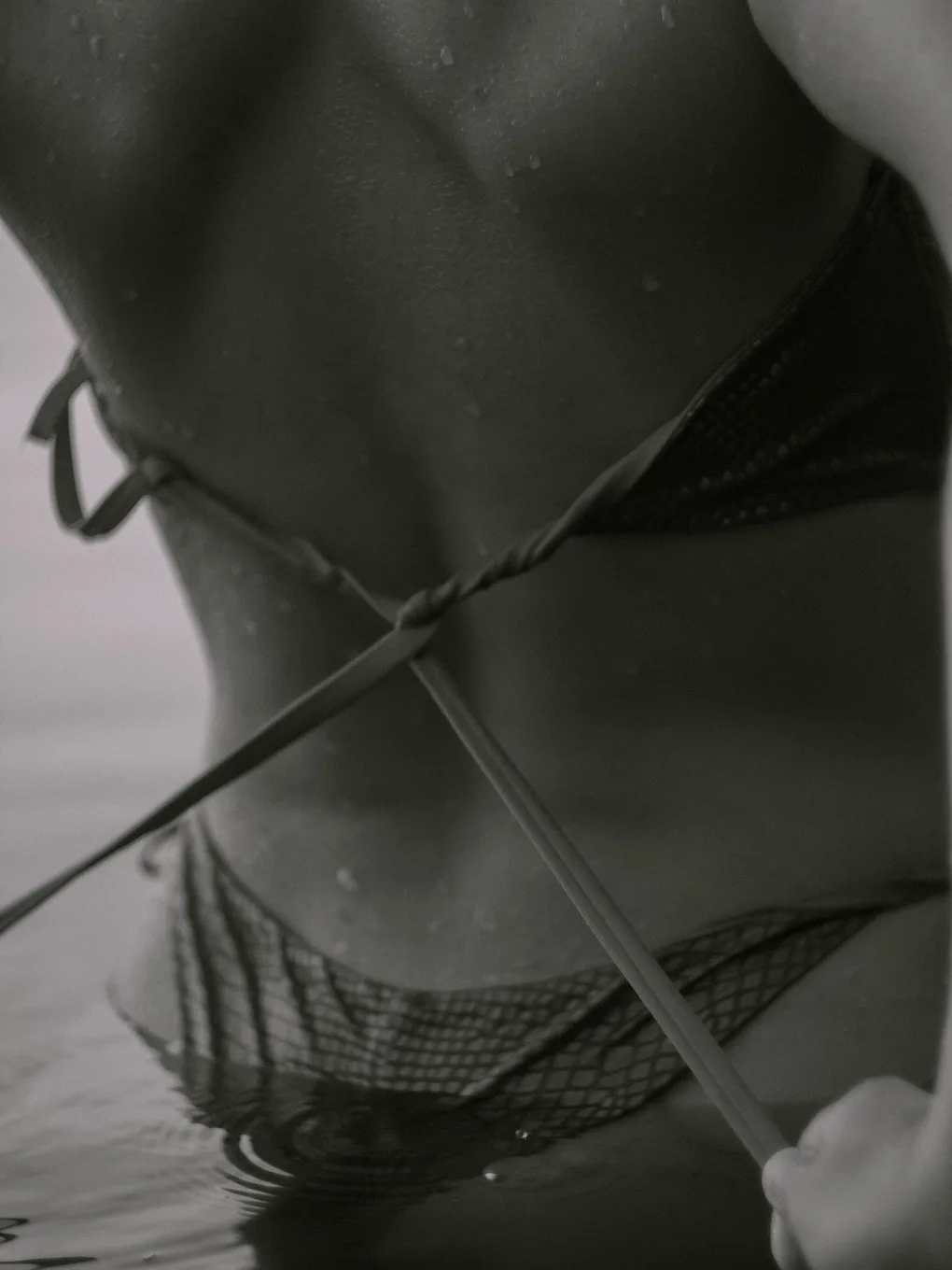Close detail of crossed swimsuit ties across a wet back, standing in still water